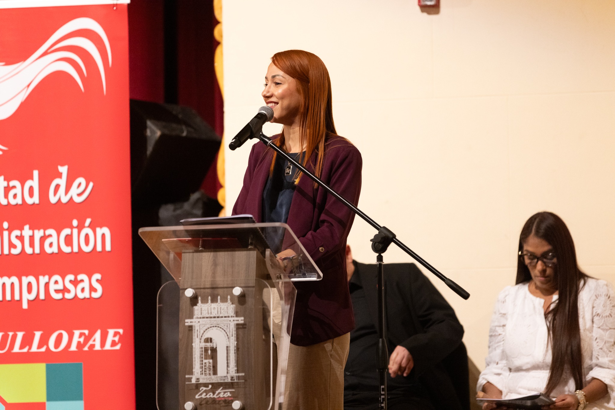 Dra. Mariluz Serrano Ortiz participa como conferenciante frente a un micrófono y un podio.